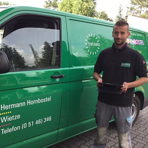 Ein junger Mann steht neben einem grünen Lieferwagen, während er ein Tablet in der Hand hält und freundlich lächelt.
