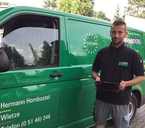 Handwerker präsentiert seine Dienstleistungen in Wietze Ein junger Mann steht neben einem grünen Lieferwagen, während er ein Tablet in der Hand hält und freundlich lächelt.