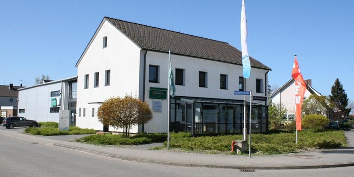 Die Fassade des Gebäudes zeigt große Fenster und ein Schild mit dem Namen 'Hornbostel', während bunte Fahnen im Wind wehen.