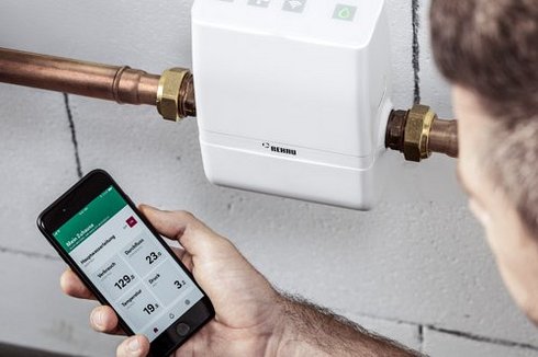 Eine Wassersteuerung und ein Mann der eine App auf dem Smartphone bedient